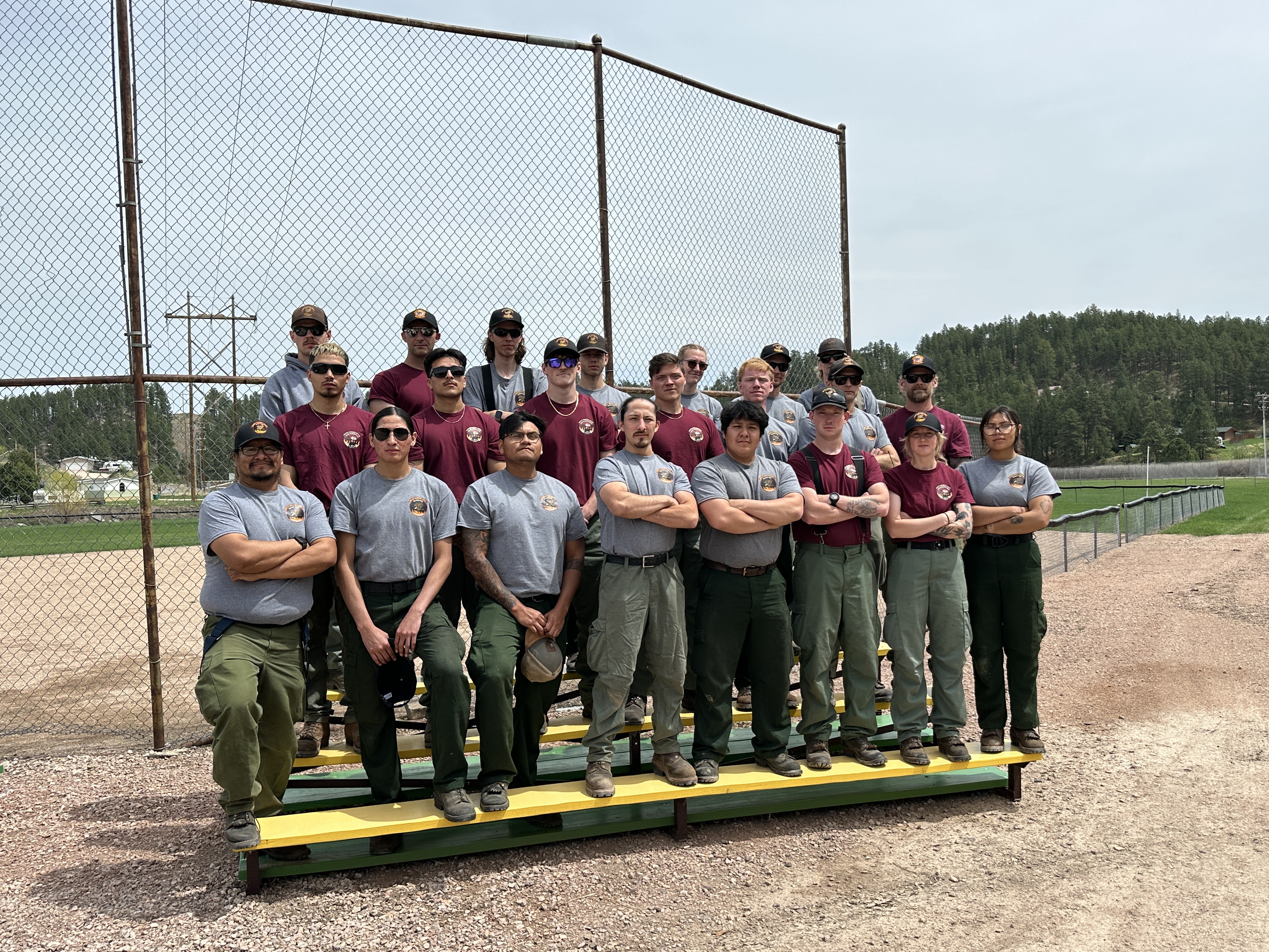 Image of South Dakota Wildland Fire handcrew members standing on bleachers in front of a softball fance