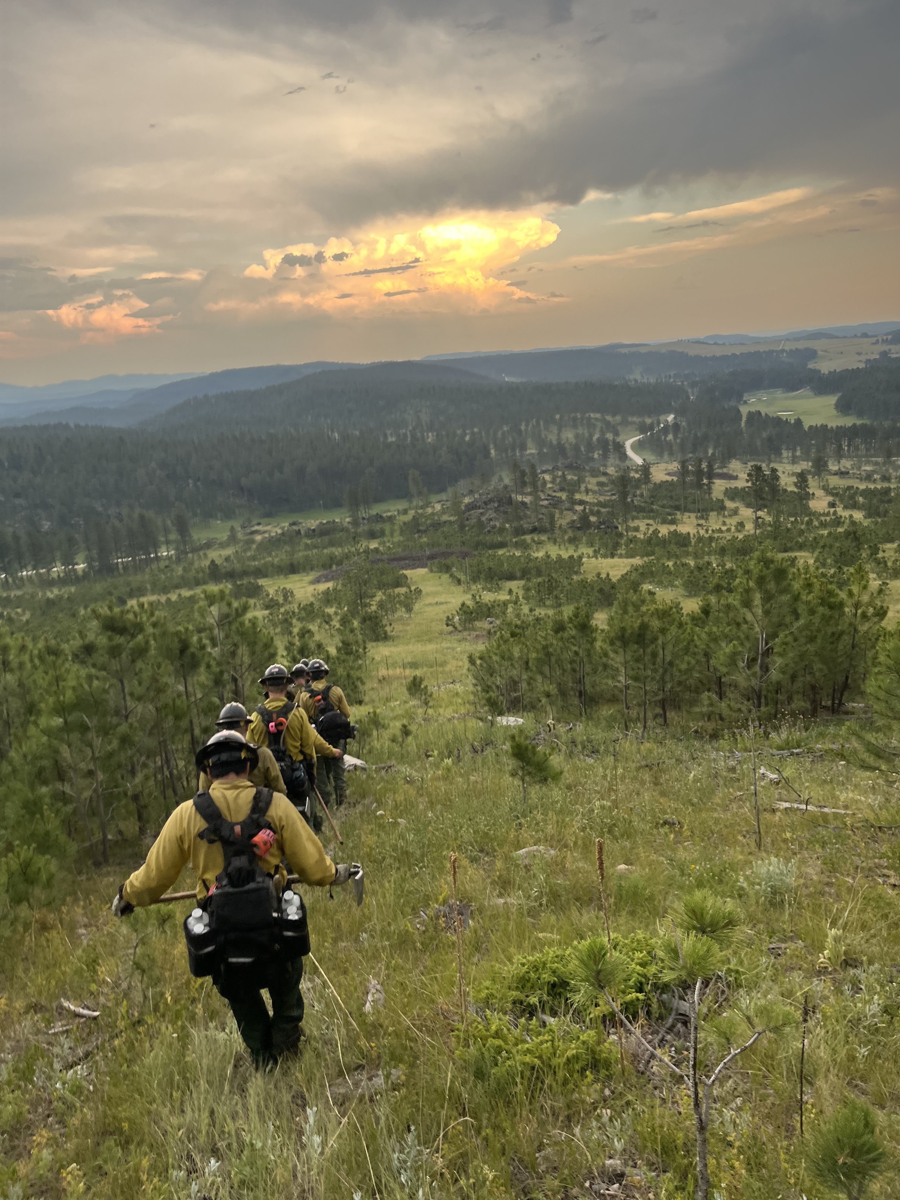 Image of Wildland Fire Black Hat crew walking down a hill during sunset